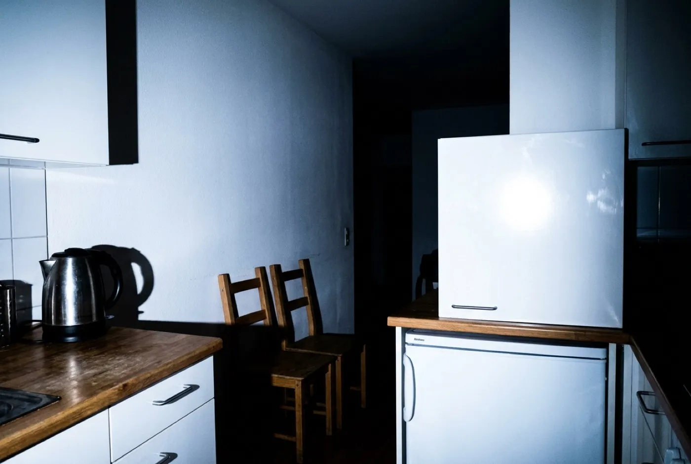 Küche mit direktem Blitz fotografiert — grelle Reflexionen auf den Fronten, harte Schatten, dunkler Hintergrund.